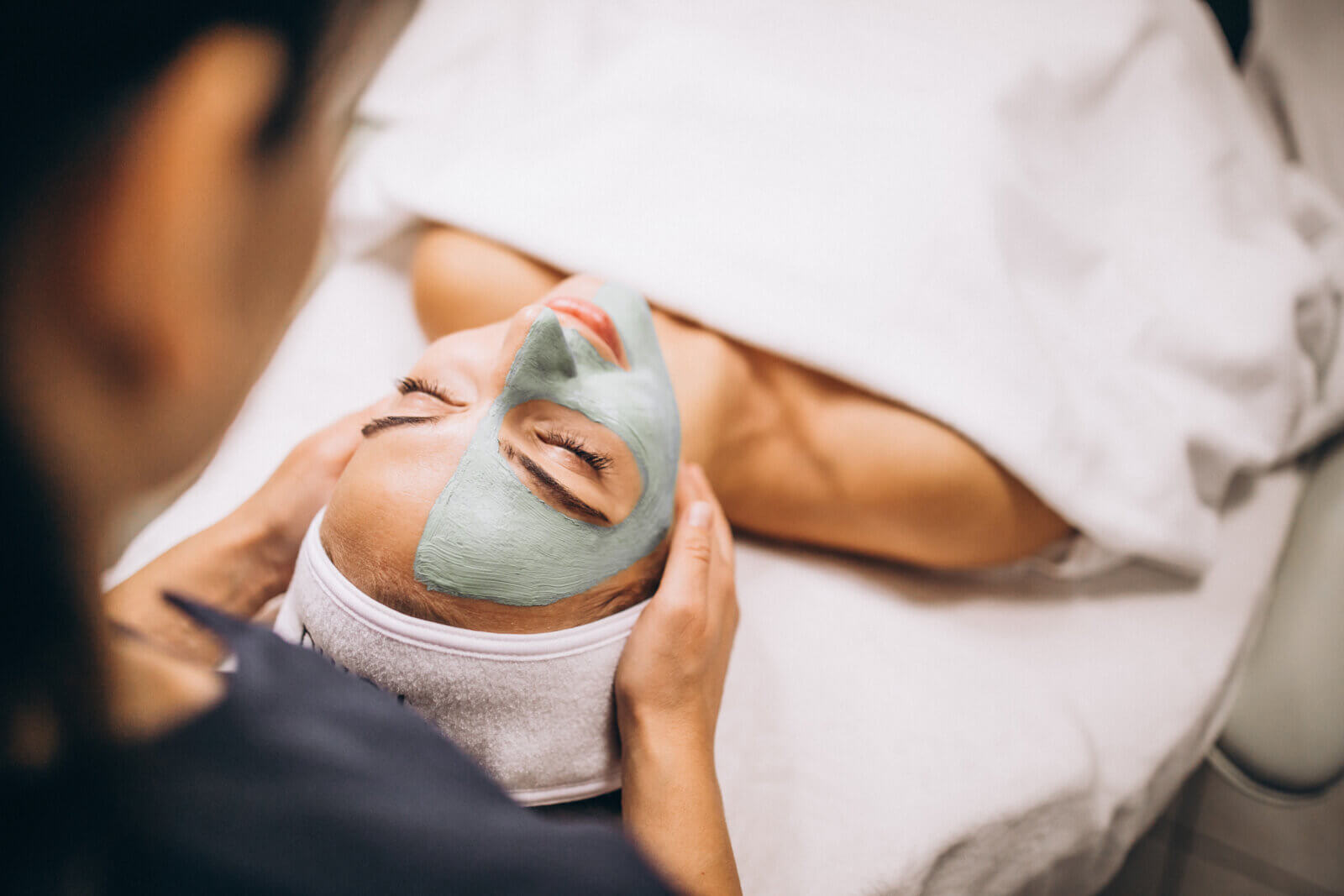 A cosmetologist applying a mask to a client's face at a beauty salon, representing the growth and demand in the dermatology segment.